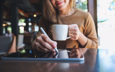 Closeup of a young woman using smart pen technology for working and writing on digital tablet screen while drinking coffee