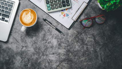 Office desk table with analysis chart or graph, pen, cup of coffee and calculator on dark background. Top view with copy space. Working desk table concept.