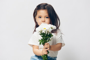 portrait of a cute, pleasant little girl with a bouquet of daisies in her hands smelling flowers, standing in a white T-shirt on a light background