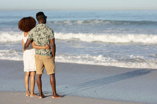 A mixed race couple admiring the view and holding each other on beach