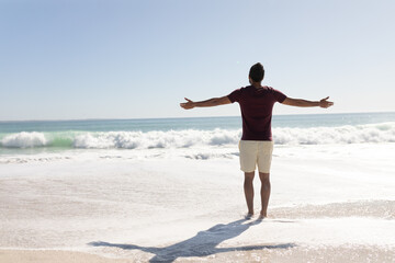 Young mixed race man raising arms on the beach