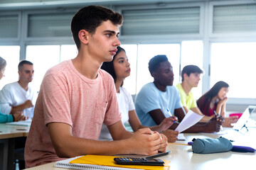 Caucasian teen male high school student in class. Multiracial university students in classroom....
