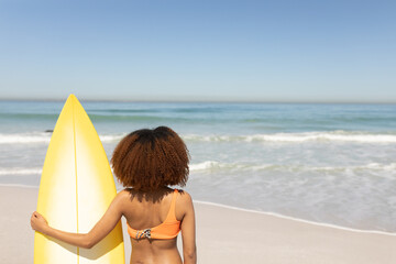 Mixed race woman holding a surfboard  on the beach
