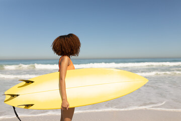 Fototapeta na wymiar Mixed race woman holding a surfboard on the beach