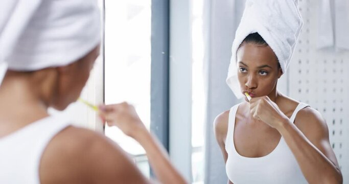 Woman cleaning and brushing teeth with a dental toothbrush at the bathroom mirror at home in the morning. Portrait of a healthy young person doing lips, mouth and dental care for a fresh white smile