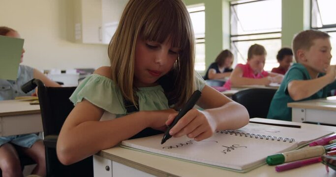 Physically challenged girl writing in her notebook in the class