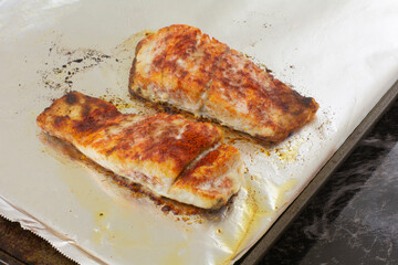 Two baked barramundi fish fillet slices with paprika spice rub on aluminum foil lined baking sheet pan