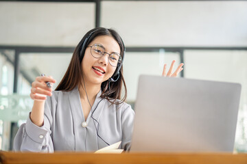 Pretty Asian woman and headphones using laptop in coffee shop writing notes. Attractive female student learning language. View webinars online. audio course education