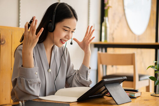 Attractive young Asian woman wearing headphones working on tablet in cafe online learning concept