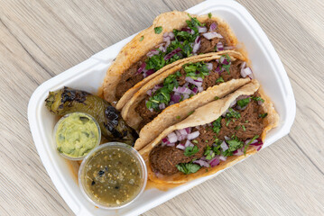 Overhead view of loaded slow cooked birria meat tacos topped with onions and served with a grilled...
