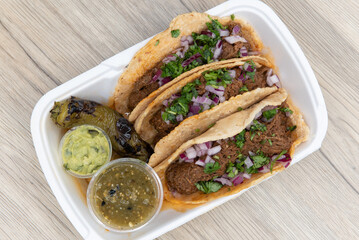 Overhead view of loaded slow cooked birria meat tacos topped with onions and served with a grilled jalapeno, salsa, and guacamole