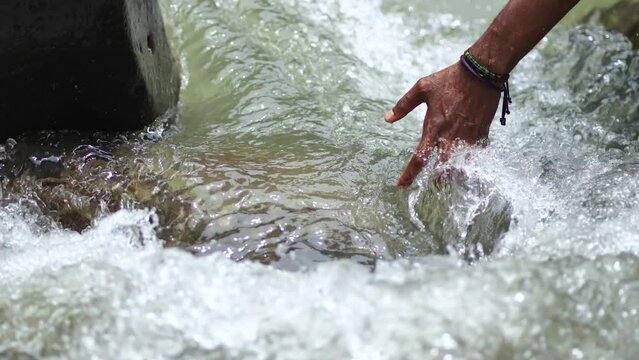 A Black Hands Touching the Flow of Water in the River