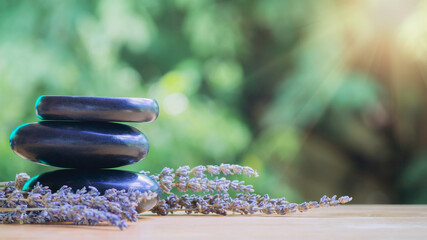 Obraz na płótnie Canvas Balance and wellness or health concept with pile of black spa stones on wood and spikes of flowering lavender with aromatherapy. Side view and landscape composition feel relaxed.