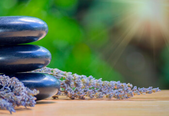 Fototapeta na wymiar Balance and wellness or health concept with pile of black spa stones on wood and spikes of flowering lavender with aromatherapy. Side view and landscape composition feel relaxed.