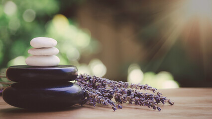 Obraz na płótnie Canvas Balance and wellness or health concept with pile of black spa stones on wood and spikes of flowering lavender with aromatherapy. Side view and landscape composition feel relaxed.