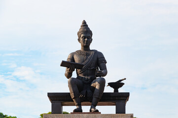 Fototapeta premium King Ramkhamhaeng Monument in Sukhothai Historical Park, Thailand. Ancient Thai king statue holding scripture with traditional attire under blue sky, famous cultural landmark 