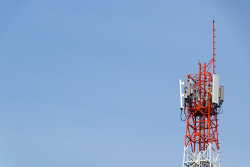 Red and white communication tower with multiple antennas against a clear blue sky, used for broadcasting, cellular network, and telecommunication signals