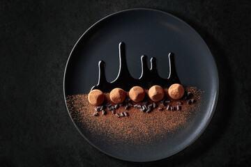 Chocolate truffles on a black plate with chocolate sauce.