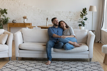 In fashionable living room carefree wife and smiling husband hugging, daydreaming spend pastime at...