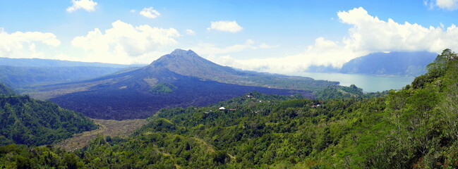 Fototapeta premium Panorama von Vulkan und See Batur in Bali mit schwarzen Lavafeldern und grünem Wald unter blauem Himmel 