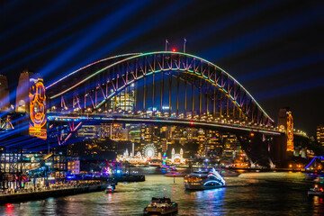 Obraz na płótnie Canvas 冬のシドニーのイベント・ビビッドシドニーで見た、青や黄色にライトアップされるハーバーブリッジと周辺の夜景