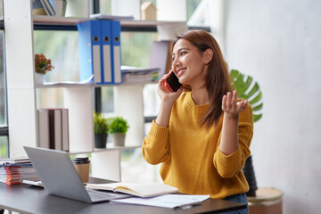Obraz premium Beautiful Asian business woman chatting on the phone with customer and working on her laptop and taking note enthusiastically and happily in the office.