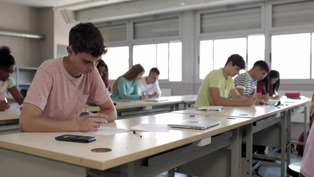 Group of college students doing an exam sitting in a row in class. Teenage guys and girls studying at high school. Education and final test concept. High quality 4k footage