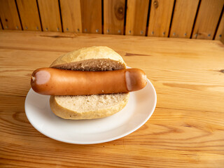 Boiled sausage with a bun on a wooden background.