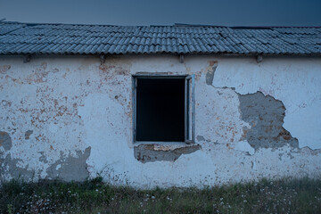 An old sinister abandoned house. The house has an empty black window. Cracked plaster