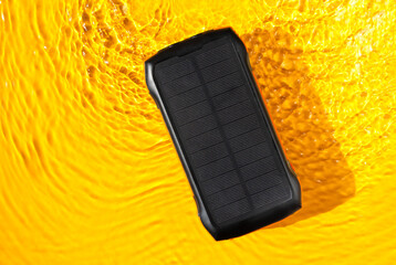 Portable power bank with solar panel lies by the water, accumulates solar energy during traveling. Alternative eco energy producing.