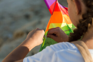 A girl collects a bright kite on sunny summer day close-up.