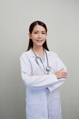 A beautiful Asian female doctor standing with her arms crossed and smiling. and put the headphones on her shoulder wearing a white coat.