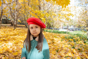 Portrait Cute child in red beret and green knitted coat against the background of yellow leaves the autumn forest. Autumn mood and concept.