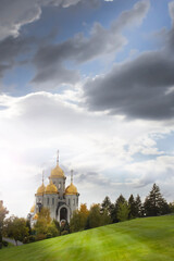 Orthodox church on a hill, golden domes. A landscape with green grass, a beautiful cloudy sky and a church. Vertical orientation