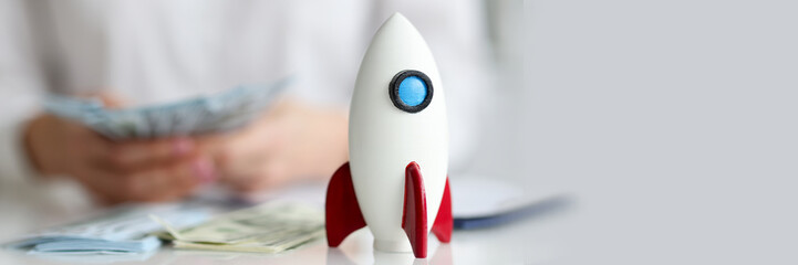 Toy rocket standing on table in front of woman with money closeup