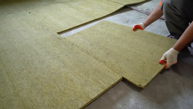 The builder insulates the floors of the house with glass wool. Laying glass wool on a concrete floor.
