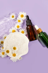 Cosmetic bottle with pipette and water drops on pastel purple viloet  background with chamomile flowers. Concept of natural moisturizing cosmetics for skin care, herbal, organic, flyer