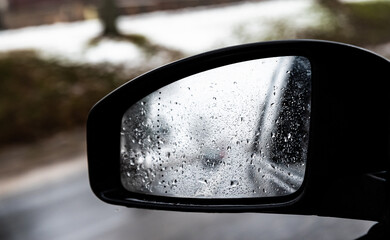 Car side mirror with water drops. Autumn weather. Cooling down and road conditions.