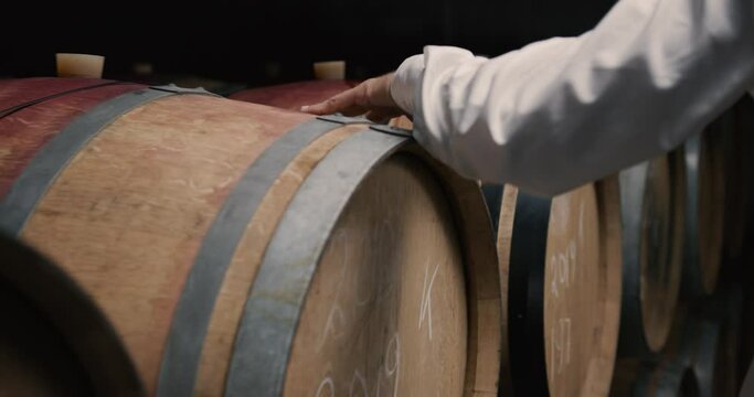 Male owners hand on Wooden oak whiskey, wine, cognac, brandy or beer barrels. A Wine Cellar. Storage Room for Wine in Bottles and Barrels.