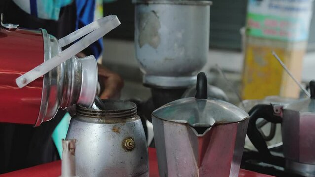 A street vendor is preparing tea, pouring hot water from termos and close it, a bit old and authentic kettles and teapot in the shoot. High quality 4k footage