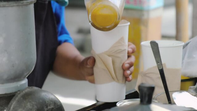 Thai tea-making process in Thailand, spilling tea in a cup, closing the cup and putting it in the bag, black gloves, no faces, light bright colors. High quality 4k footage