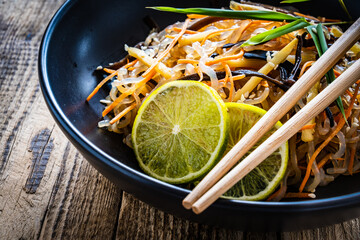Asian food - konjac noodles, stir fried vegetables, soy sauce and mushrooms on wooden table
