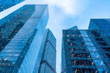 The tops of modern corporate buildings in snowfall. Low angle view of skyscrapers.