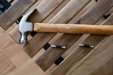 a hammer on top of a wooden chair, behind it a plank part of a gray desk.