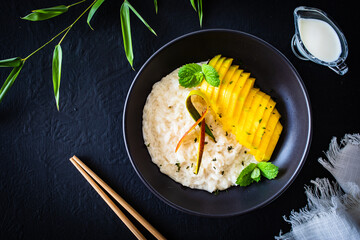 Rice in coconut milk with mango and mint on black wooden table