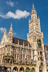 Fototapeta premium Die im Stil der Neugotik gestaltete Fassade des neuen Rathaus mit Rathausturm in der Altstadt von München in Unteransicht vom Marienplatz aus gesehen bei schönem Sommerwetter und blauen Himmel