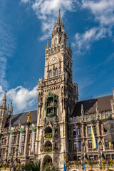 Fototapeta na wymiar Die im Stil der Neugotik gestaltete Fassade des neuen Rathaus mit Rathausturm in der Altstadt von München in Unteransicht vom Marienplatz aus gesehen bei schönem Sommerwetter und blauen Himmel