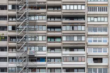 Die graue Fassade ines Wohnhochhauses mit Balkonen, einem Au&szlig;enaufzug und Fenstern in einer verdichteten Teleaufnahme