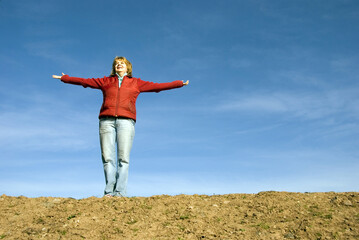 woman in red with open arms in a meadow with blue sky behind. I'm happy! concept