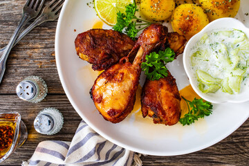 Roasted chicken drumsticks with fried potato and cucumbers in cream on wooden table

